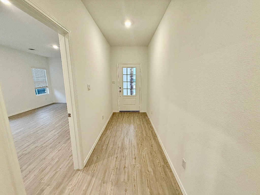1724 Four Waters Loop Georgetown, TX 78628 - Photo 3 of 38 Doorway to outside and seprarate door to the left to enter the Gen X Suite featuring baseboards and wood finished floors