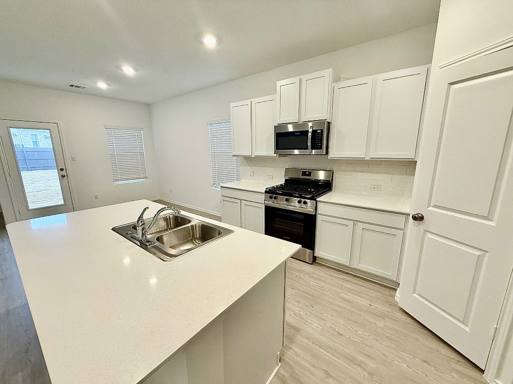 1724 Four Waters Loop Georgetown, TX 78628 - Photo 4 of 38 Kitchen with appliances with stainless steel finishes, white cabinets, decorative backsplash, light wood-type flooring, and a center island with sink