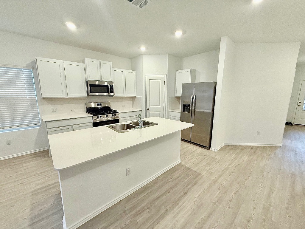 1724 Four Waters Loop Georgetown, TX 78628 - Photo 5 of 38 Kitchen with appliances with stainless steel finishes, light countertops, white cabinetry, and a kitchen island with sink