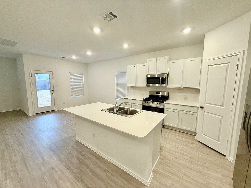 1724 Four Waters Loop Georgetown, TX 78628 - Photo 6 of 38 Kitchen featuring appliances with stainless steel finishes, white cabinets, an island with sink, light countertops, and light wood-style flooring