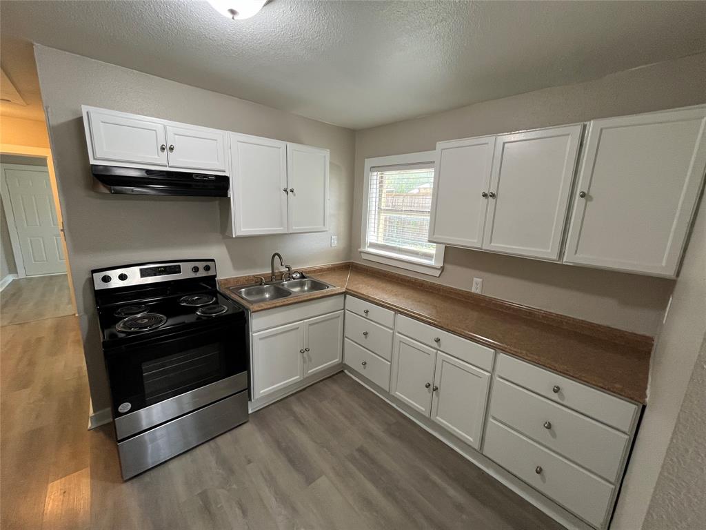 1316 North Prairie Creek Road Dallas, TX 75217 - Photo 5 of 19 Kitchen featuring white cabinetry, stainless steel range, and wood-finish flooring