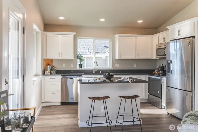 a kitchen with stainless steel appliances granite countertop a stove a sink dishwasher a refrigerator and white cabinets with wooden floor