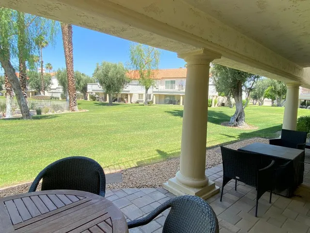a view of a patio with lawn chairs floor to ceiling window next to yard and a road