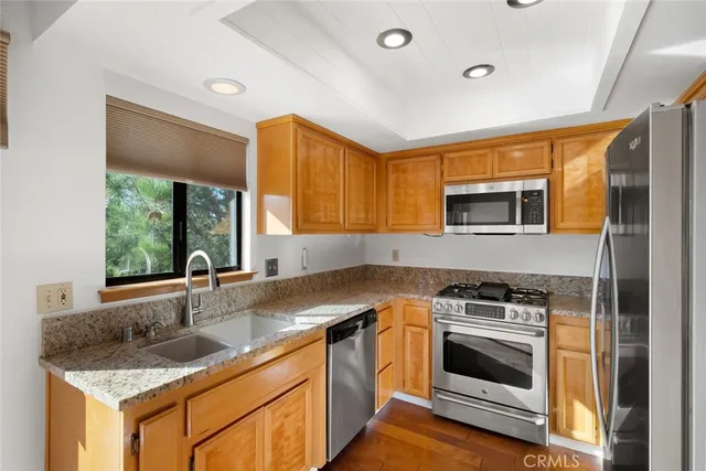 a open kitchen with stainless steel appliances granite countertop a refrigerator a stove and a sink with cabinets