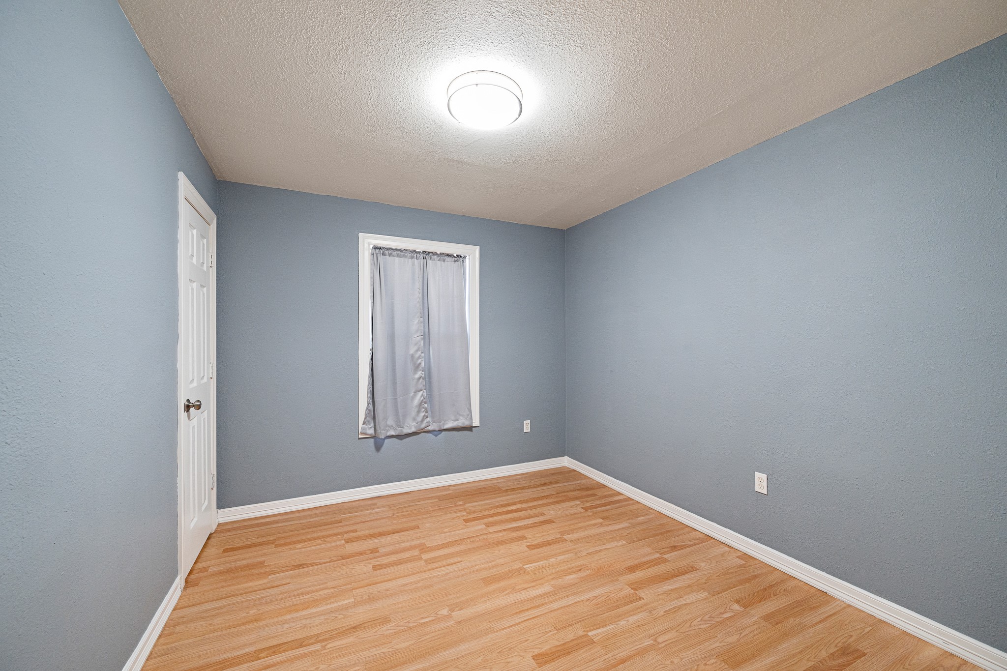 7815 Harding Street, Unit B Houston, TX 77012 - Photo 19 of 21 Discover the charm of Bedroom 2, featuring soothing blue walls, warm flooring, and soft natural light, creating a serene and inviting retreat.