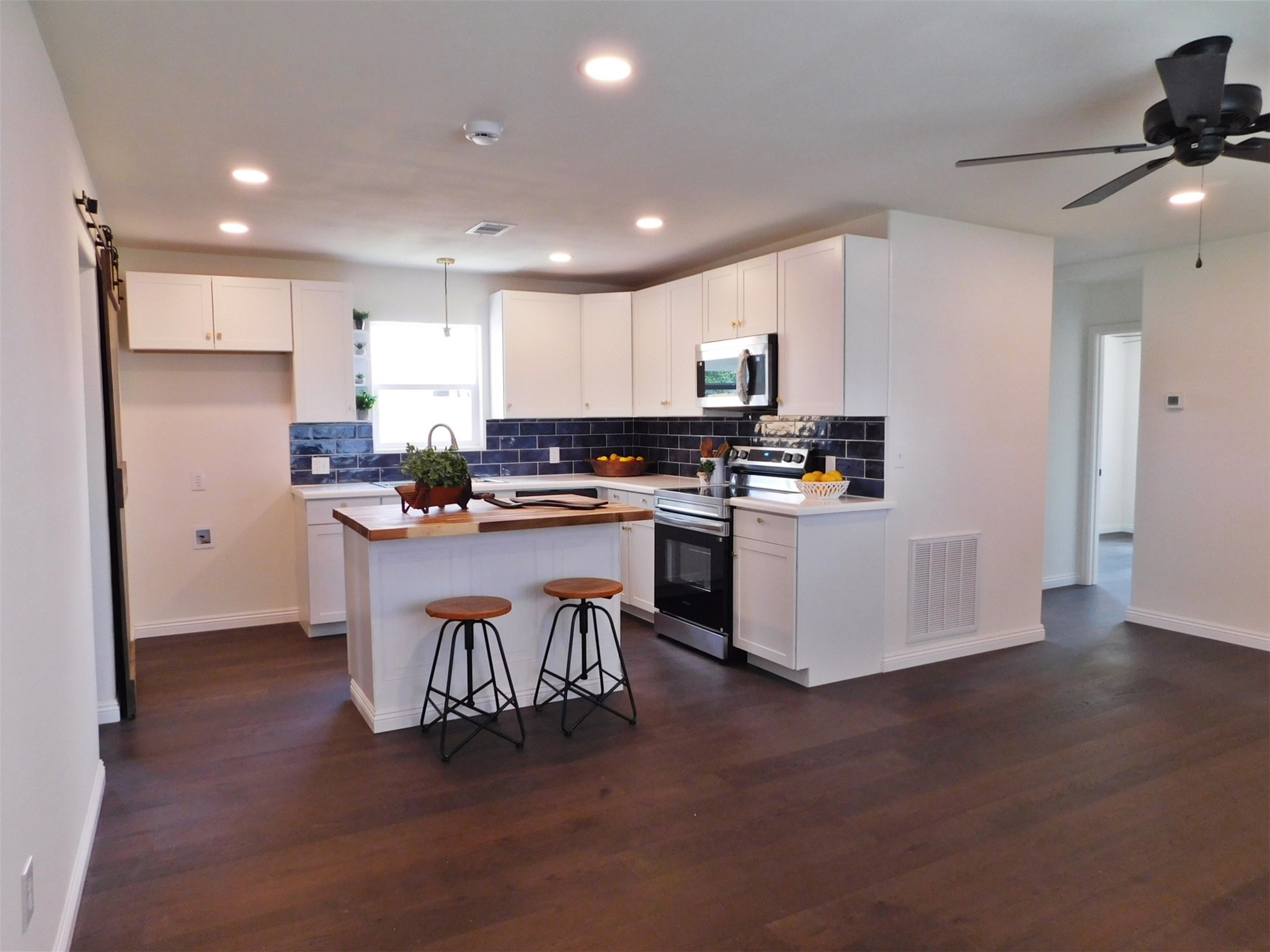 205 East Train Street Ellinger, TX 78938 - Photo 8 of 27 a kitchen with stainless steel appliances a microwave a stove a sink a refrigerator and white cabinets with wooden floor