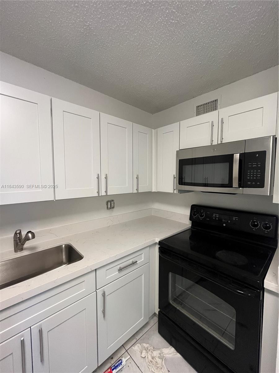 7430 Southwest 153rd Place, Unit 1061 Miami, FL 33193 - Photo 7 of 42 a kitchen with white cabinets and black appliances