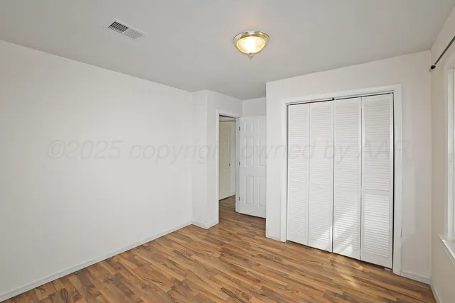a view of an empty room with wooden floor and closet
