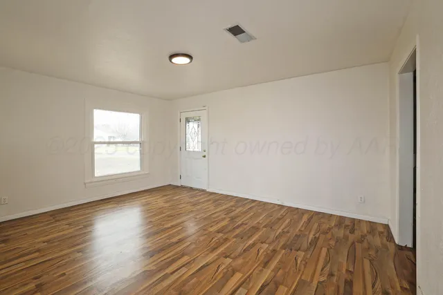 a view of an empty room with wooden floor and a window
