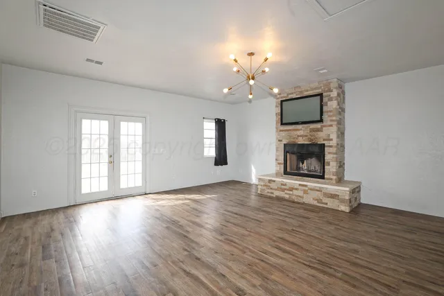 an empty room with wooden floor fireplace and chandelier