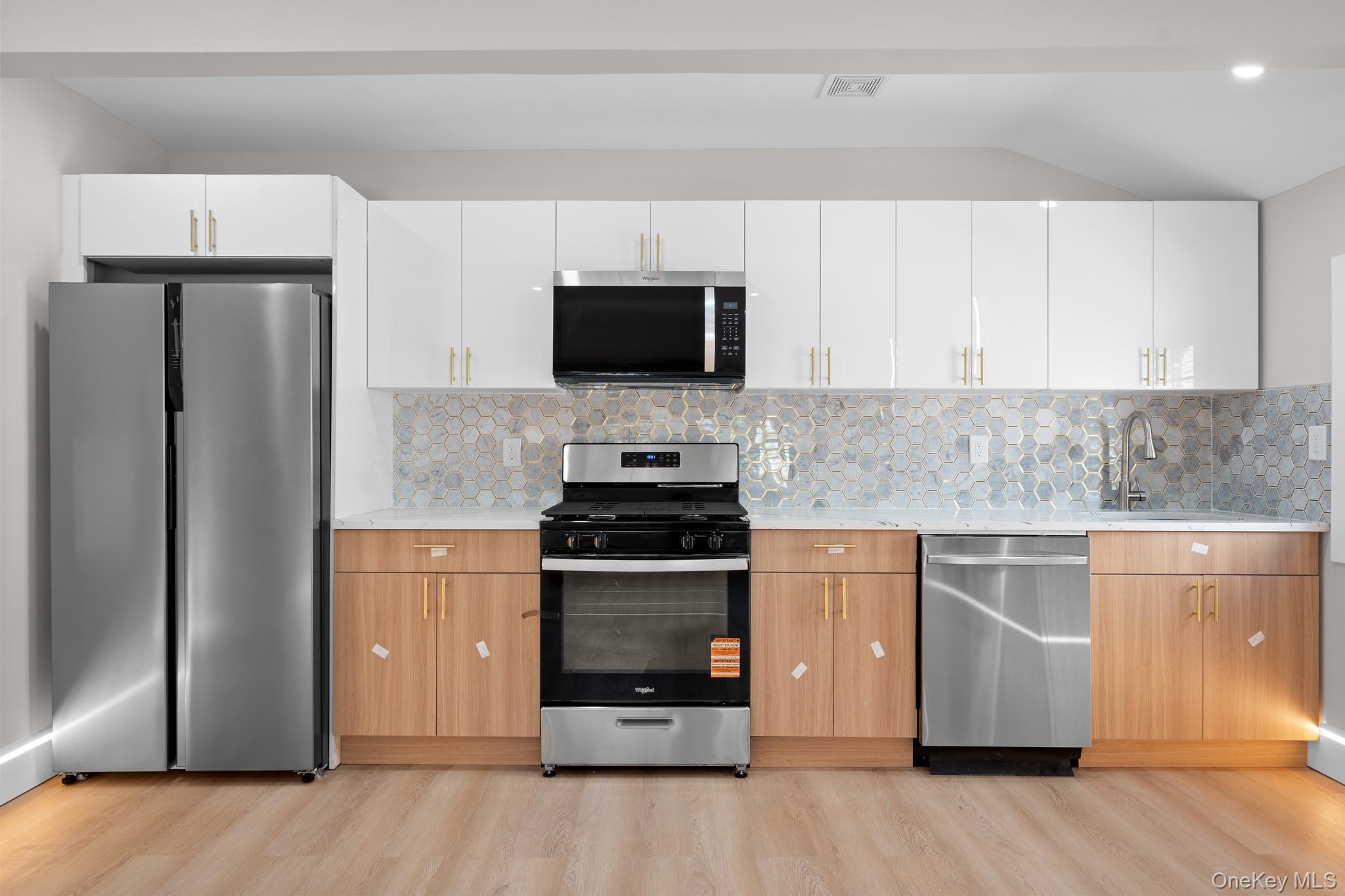 115-16 199th Street Queens, NY 11412 - Photo 11 of 21 Kitchen with appliances with stainless steel finishes, tasteful backsplash, light stone countertops, white cabinets, and vaulted ceiling