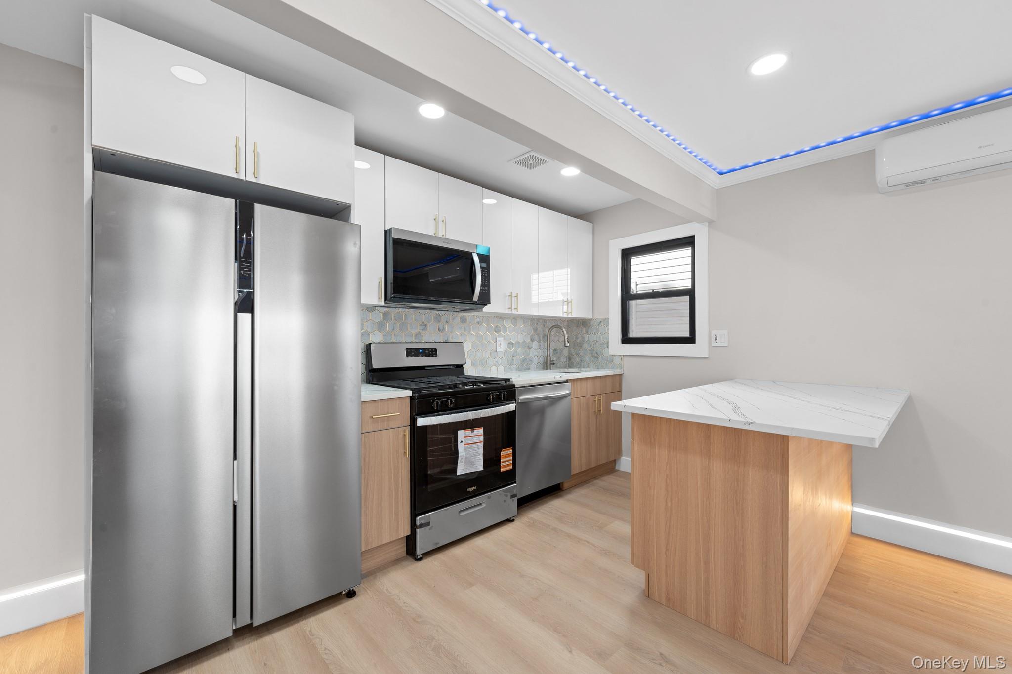 115-16 199th Street Queens, NY 11412 - Photo 2 of 21 Kitchen featuring stainless steel appliances, white cabinetry, light wood-type flooring, a peninsula, and decorative backsplash