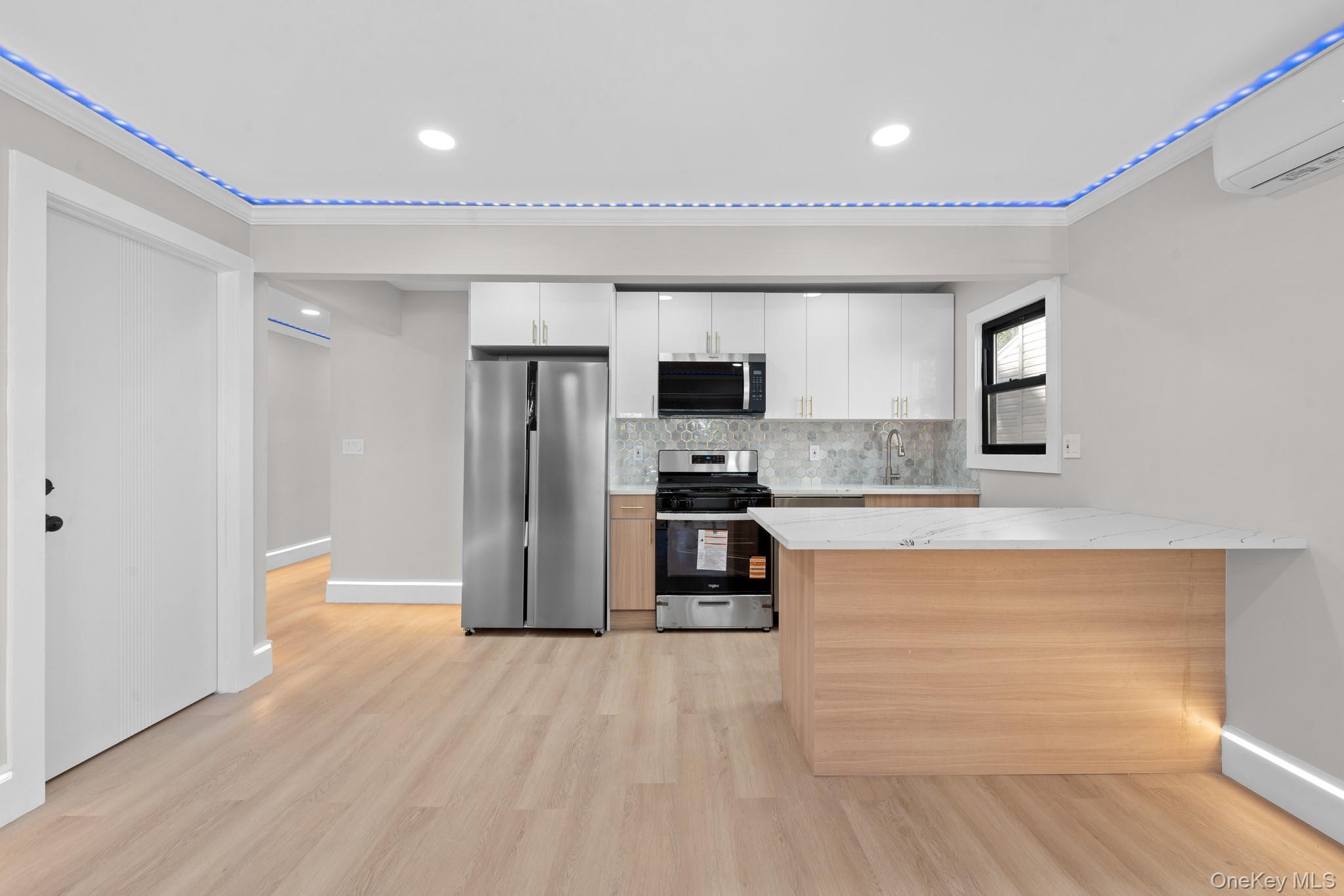 115-16 199th Street Queens, NY 11412 - Photo 3 of 21 Kitchen with white cabinets, appliances with stainless steel finishes, backsplash, an AC wall unit, and light wood-type flooring