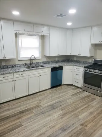 a large kitchen with granite countertop a stove top oven a sink and white cabinets