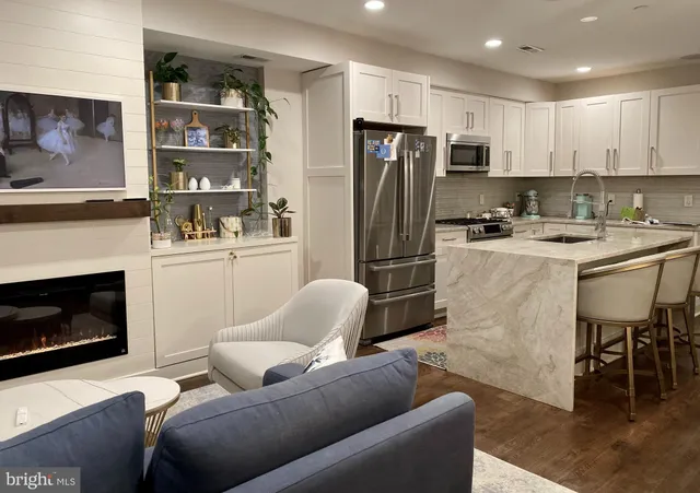a living room with stainless steel appliances furniture a fireplace a flat screen tv and a window