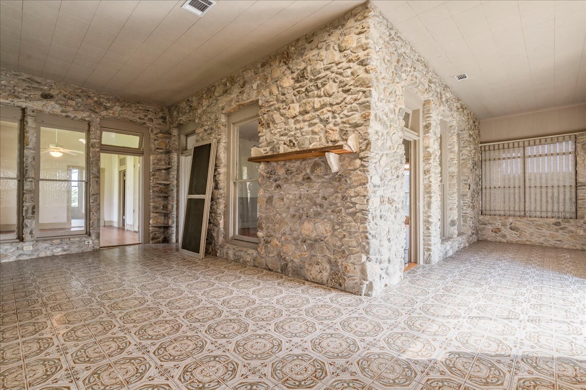 6400 Cypress Road Kyle, TX 78640 - Photo 17 of 33 Stone-clad sunroom featuring patterned floor tiles, multiple window openings, and a wood shelf