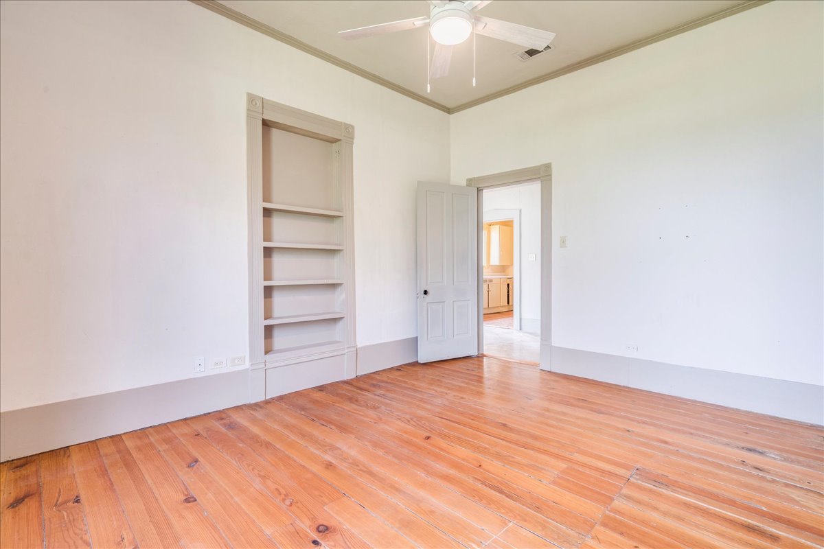 6400 Cypress Road Kyle, TX 78640 - Photo 23 of 33 Spacious room featuring wood flooring, neutral wall tones, a built-in shelving unit, a ceiling fan fixture, and a solid panel door with dark hardware