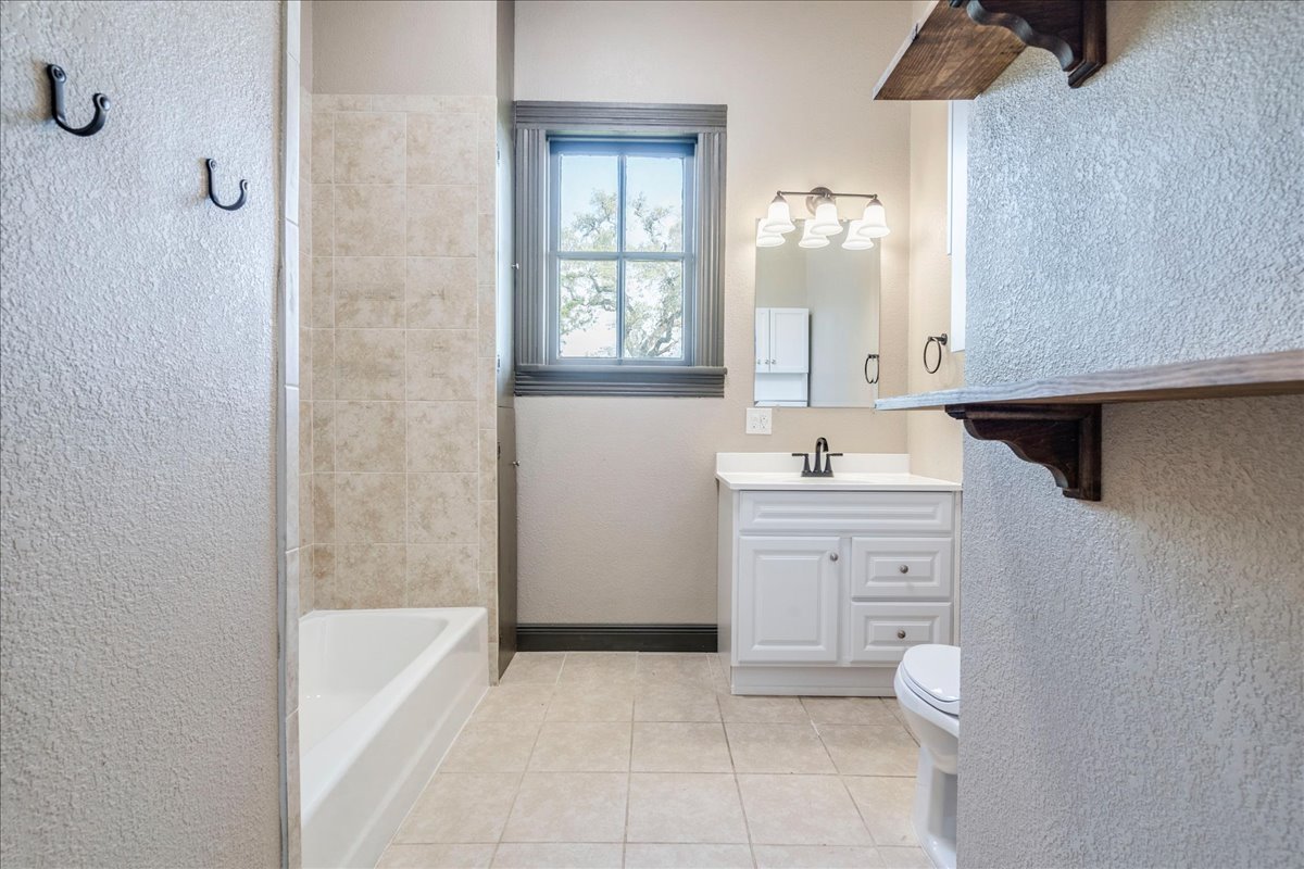 6400 Cypress Road Kyle, TX 78640 - Photo 24 of 33 Bathroom featuring a white vanity with integrated sink, tiled flooring, a bathtub with tiled surround, a window with dark trim, and decorative wood shelving