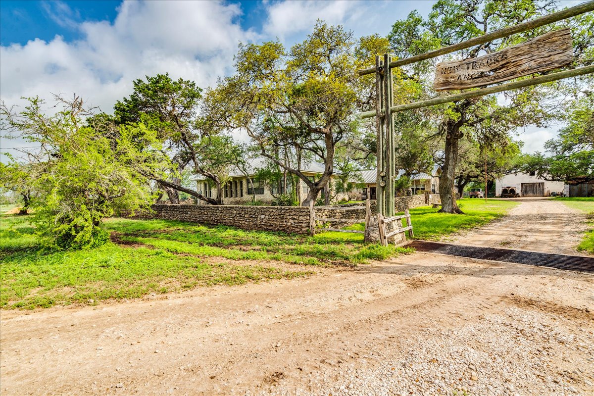 6400 Cypress Road Kyle, TX 78640 - Photo 31 of 33 Rustic wooden entry gate with a carved wooden sign, a gravel driveway, and a stone wall