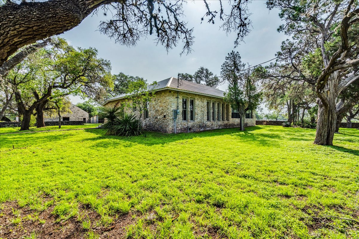 6400 Cypress Road Kyle, TX 78640 - Photo 7 of 33 Stone exterior residence featuring multiple windows, a sloped roof, and mature trees encompassing the property