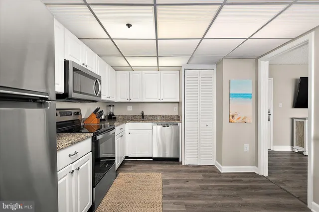 a kitchen with stainless steel appliances granite countertop a stove a refrigerator a sink dishwasher and white cabinets with wooden floor