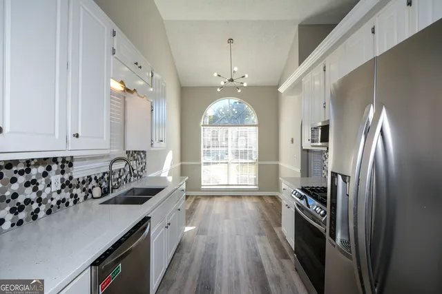 a kitchen with stainless steel appliances granite countertop a refrigerator a sink dishwasher a stove and white countertops with wooden floor