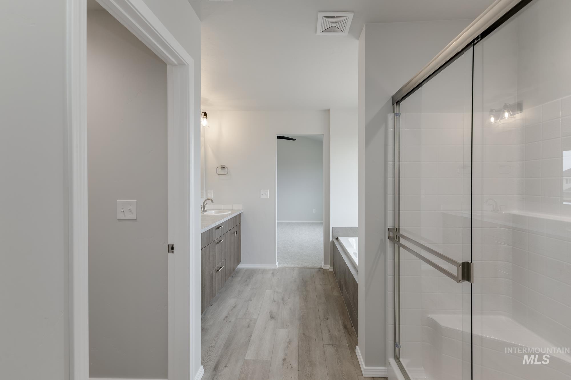 12842 Ropers Street Nampa, ID 83651 - Photo 28 of 29 Contemporary bathroom featuring a glass-enclosed shower with white subway tile, a built-in tub, dual vanity with undermount sinks, and wood-finish flooring