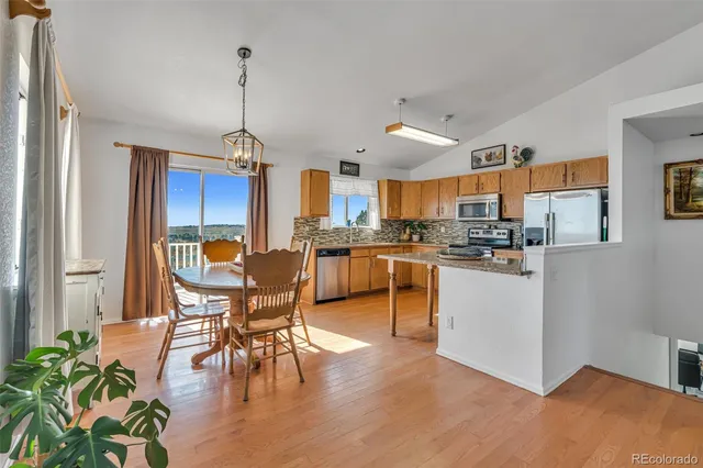 a kitchen with stainless steel appliances granite countertop a stove top oven a sink a dining table and chairs with wooden floor