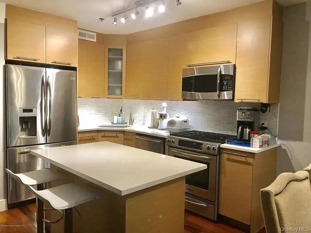 Kitchen with appliances with stainless steel finishes, light brown cabinets, light countertops, glass insert cabinets, and a kitchen breakfast bar