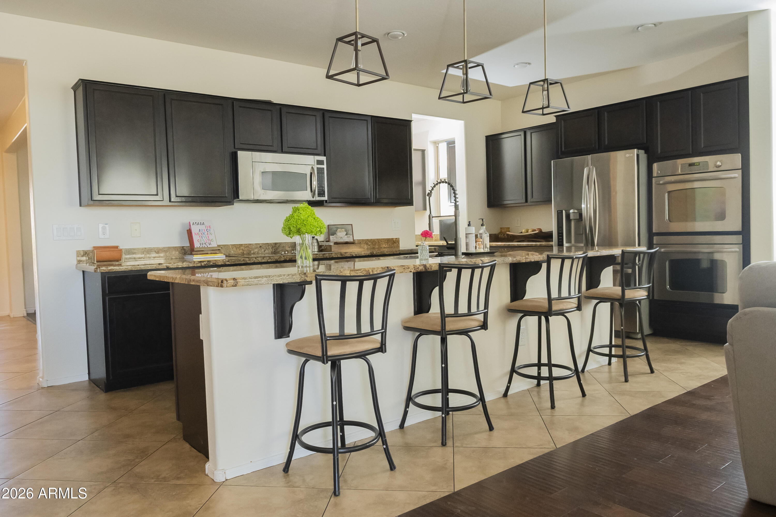 16045 West Almeria Road Goodyear, AZ 85395 - Photo 8 of 31 a kitchen with stainless steel appliances kitchen island granite countertop a table chairs microwave and sink