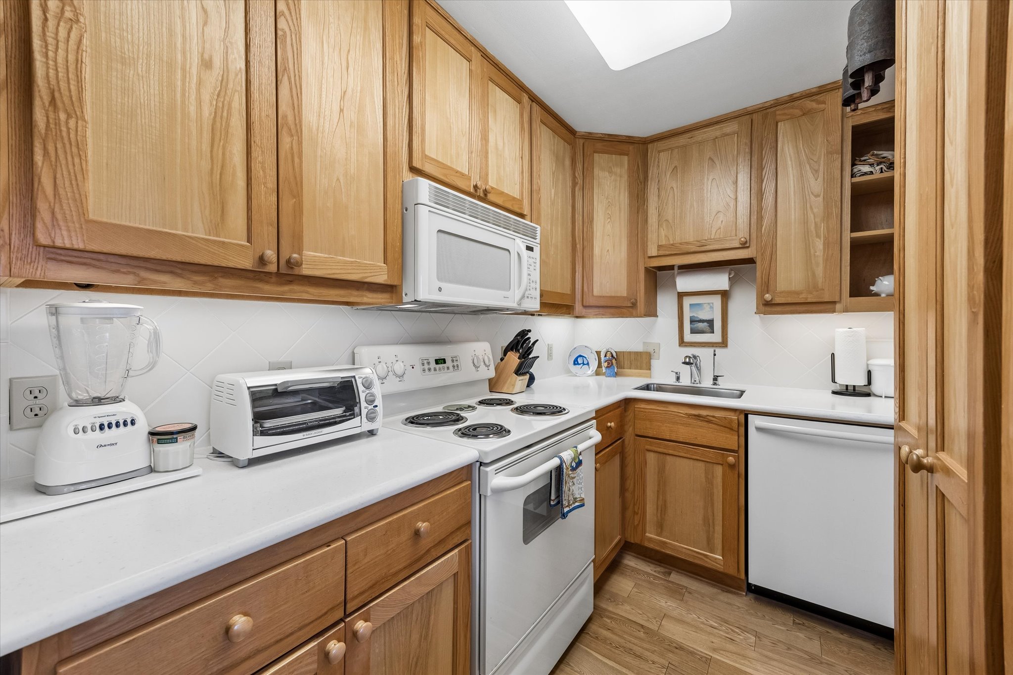 1801 Lavaca Street, Unit 3M Austin, TX 78701 - Photo 4 of 30 Kitchen with white appliances, light countertops, light wood finished floors, wood finish cabinetry, and backsplash