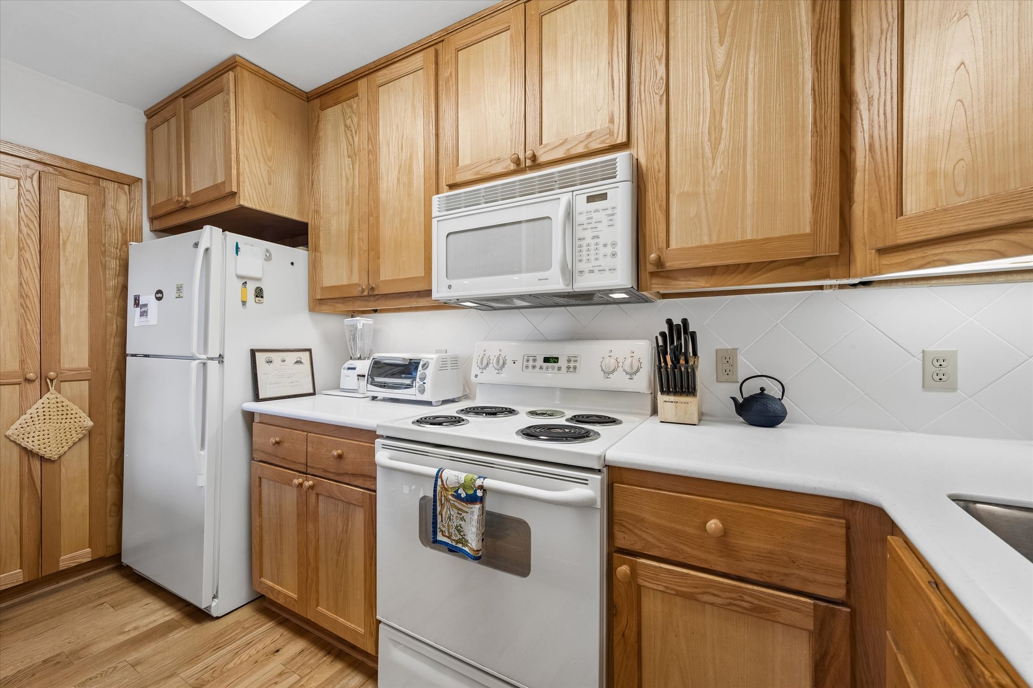 1801 Lavaca Street, Unit 3M Austin, TX 78701 - Photo 5 of 30 Kitchen featuring white appliances, light countertops, backsplash, light wood-type flooring, and wood finish cabinets