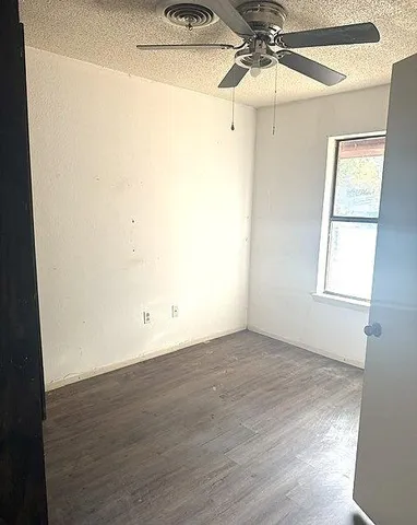 an empty room with wooden floor fan and windows