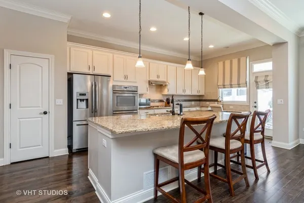 a kitchen with stainless steel appliances granite countertop a table chairs refrigerator and sink