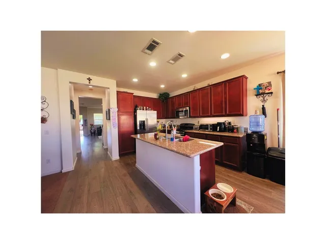 a kitchen with kitchen island granite countertop a refrigerator a stove top oven a sink dishwasher and wooden cabinets with wooden floor