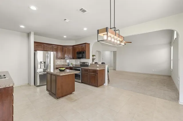 a kitchen with stainless steel appliances granite countertop a sink a stove a refrigerator cabinets and chairs