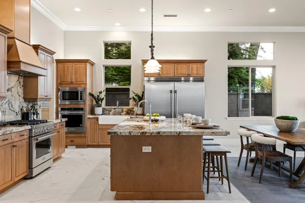 a kitchen with stainless steel appliances granite countertop a stove top oven a sink dishwasher a dining table and chairs with wooden floor