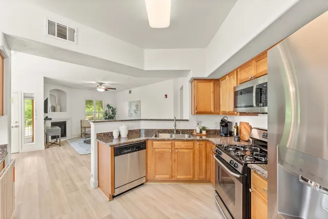 a kitchen with stainless steel appliances granite countertop a stove top oven a sink dishwasher a dining table and chairs with wooden floor