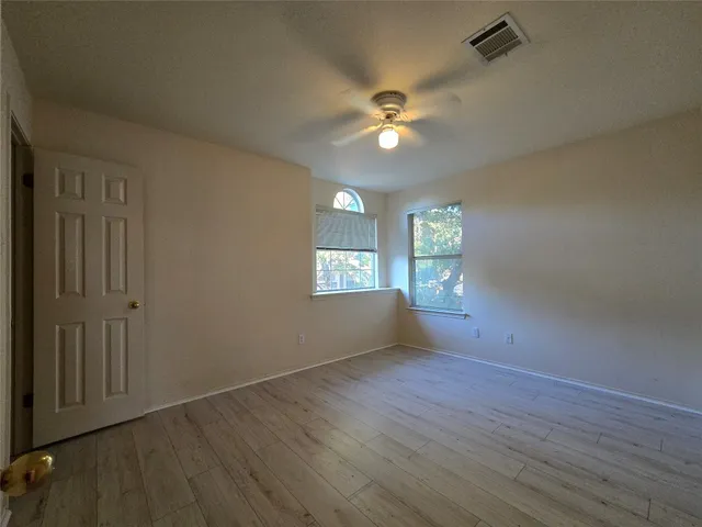 an empty room with wooden floor chandelier fan and windows