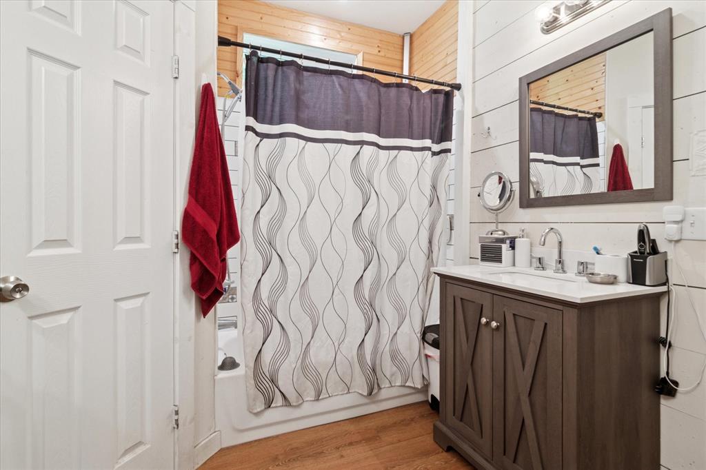 1102 West 12th Street Bonham, TX 75418 - Photo 16 of 27 Full bath featuring shower / bath combo, vanity, wood walls, and light wood-type flooring