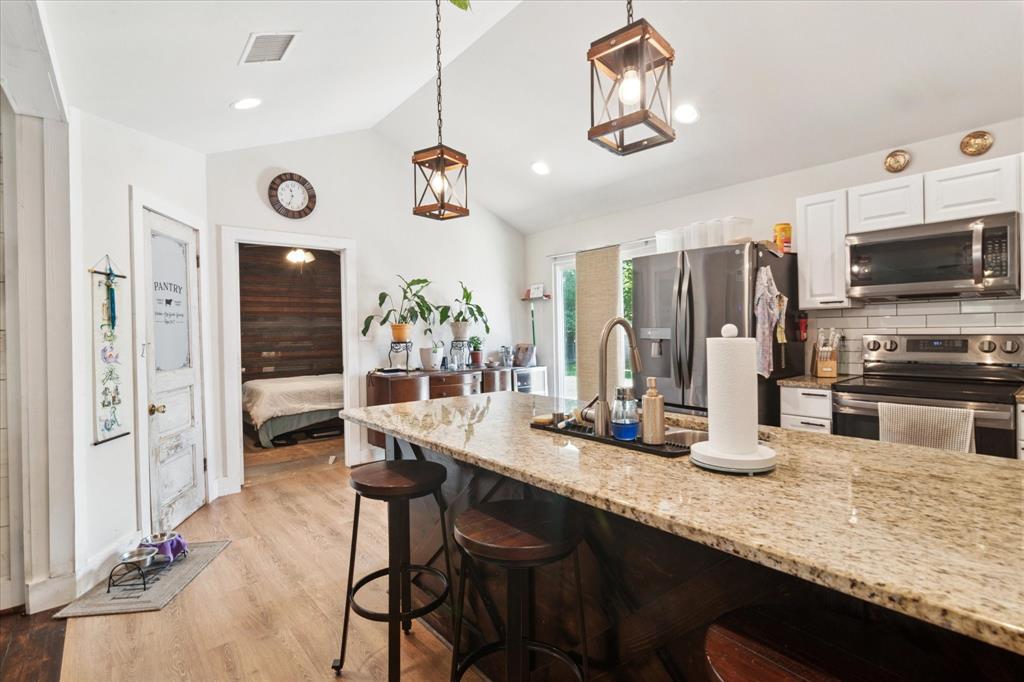 1102 West 12th Street Bonham, TX 75418 - Photo 4 of 27 Kitchen with appliances with stainless steel finishes, light stone countertops, white cabinetry, light wood finished floors, and lofted ceiling