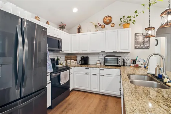 a kitchen with stainless steel appliances granite countertop a refrigerator a sink dishwasher a stove and white cabinets with wooden floor