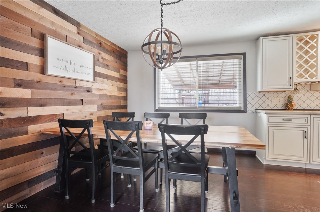 15575 Stillwell Road Huntsburg, OH 44046 - Photo 12 of 48 Dining area featuring a chandelier, a textured ceiling, dark wood-style flooring, and accent wood wall