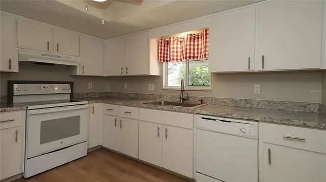 a kitchen with granite countertop white cabinets white appliances and a sink