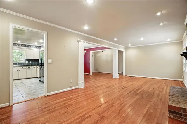 a view of an empty room with wooden floor and a kitchen