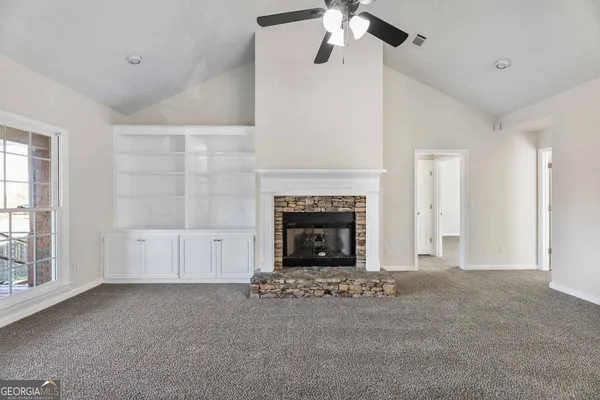 a view of a livingroom with a fireplace a ceiling fan and windows