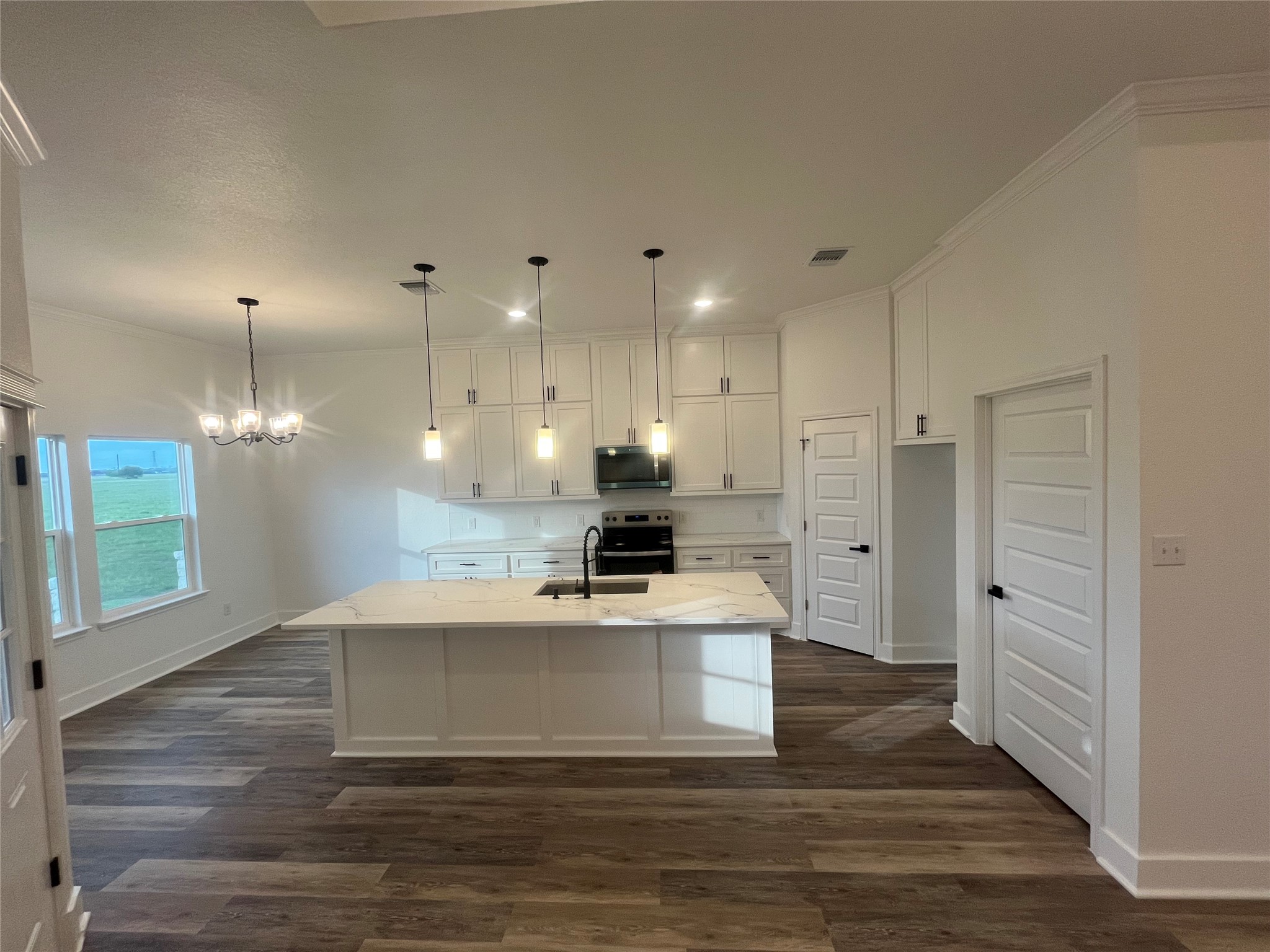33416 FM 521 Road Angleton, TX 77515 - Photo 8 of 21 This photo showcases a modern kitchen with a large island, pendant lighting, and medium gray/wood water proof plank flooring. It features white cabinetry, Black & stainless steel appliances, and ample natural light from large windows.