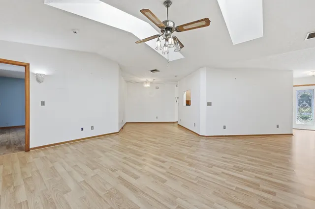 an empty room with wooden floor chandelier fan and windows