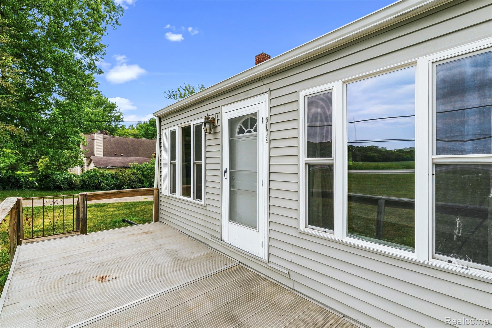 6163 North State Road Davison, MI 48423 - Photo 12 of 45 Exterior siding, multiple windows with white frames, outdoor porch lighting fixture, front entry door with transom window, and a wooden deck with metal railing
