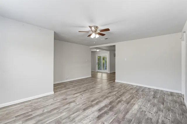 a view of an empty room with chandelier fan and wooden floor